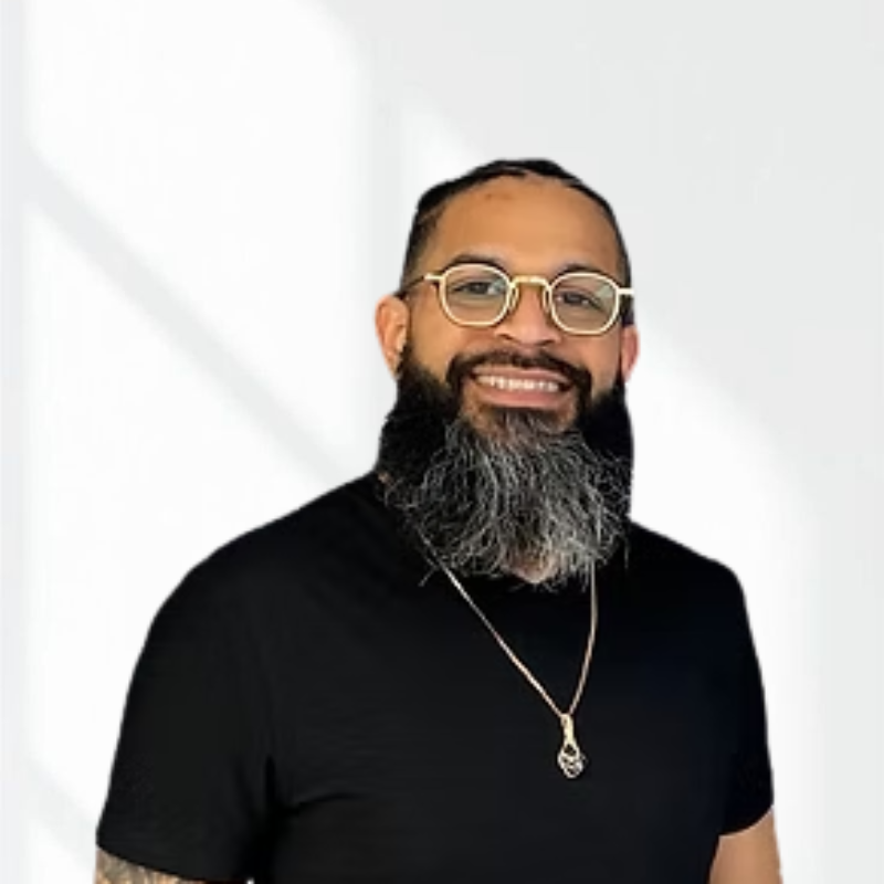 Man with glasses, beard, and a black shirt, smiling in front of a plain white background.