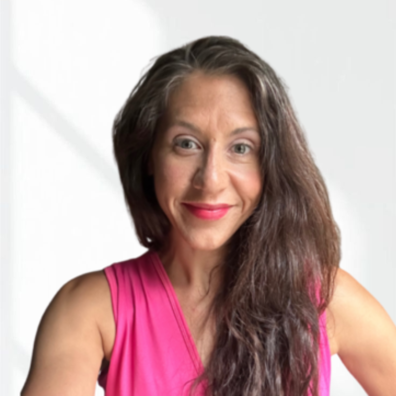 A woman with long, wavy brown hair wearing a sleeveless pink top, smiling at the camera.