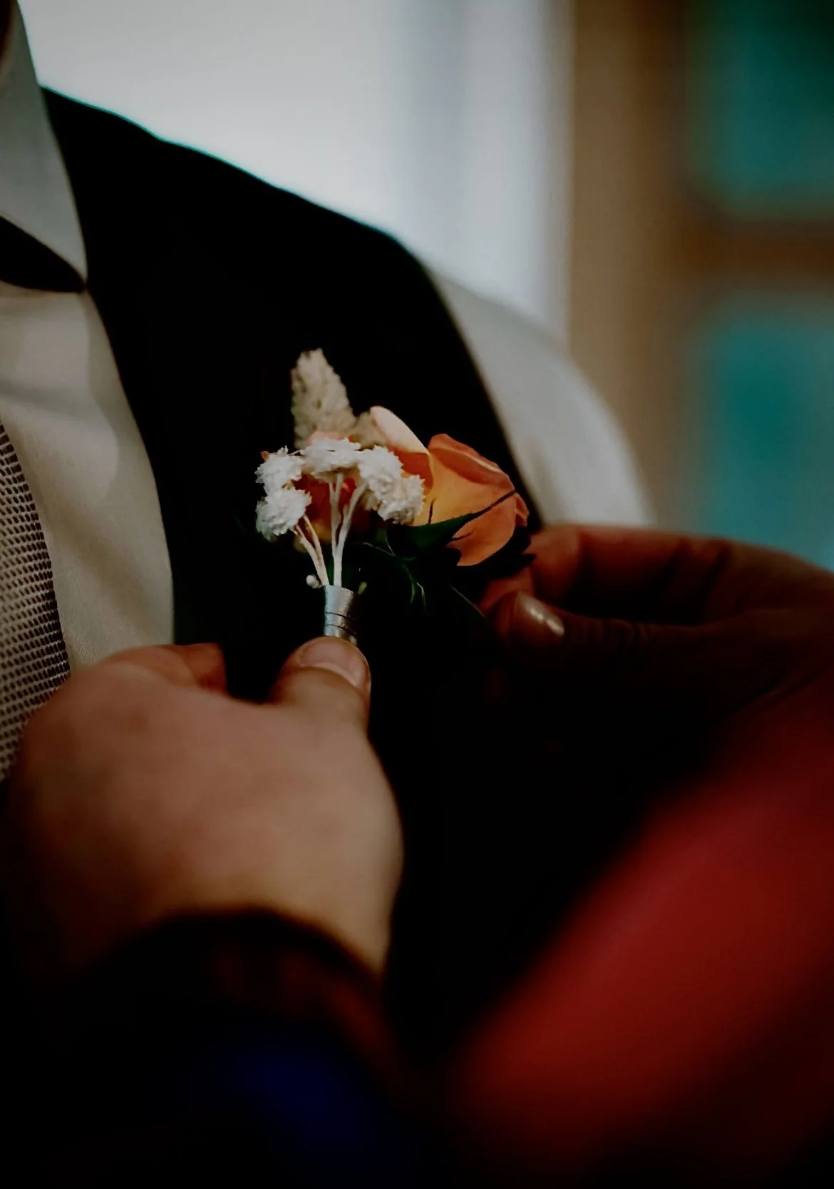 A person in a black and white suit is pinning a boutonniere made of white and orange flowers to their lapel.