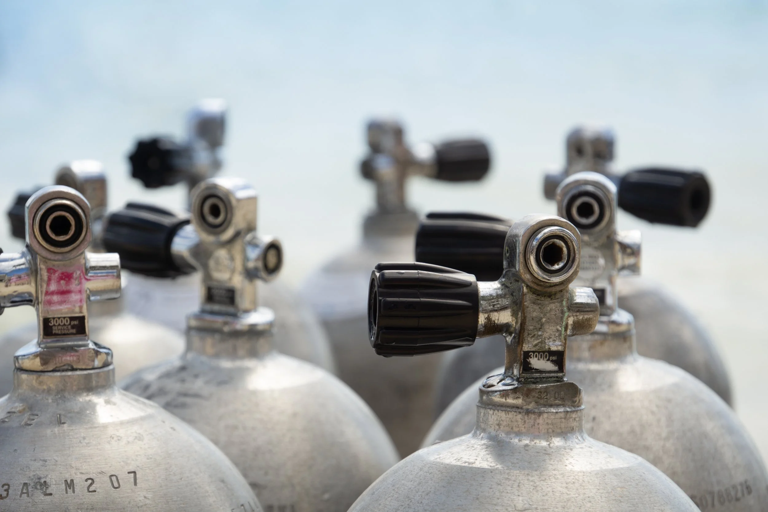 A row of scuba diving tanks with regulators and gauges inside a boat or storage area.
