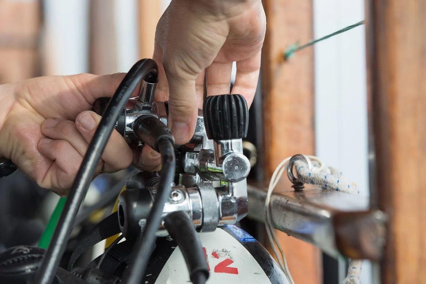 A close-up of a person's hand adjusting a gas valve on a gas tank, with plumbing and electrical wires in view.