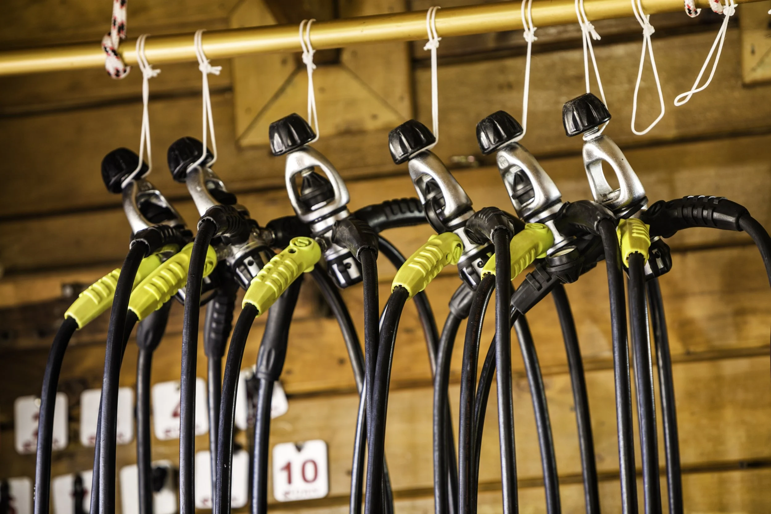 A row of scuba diving regulators hanging on hooks in a wooden storage area.