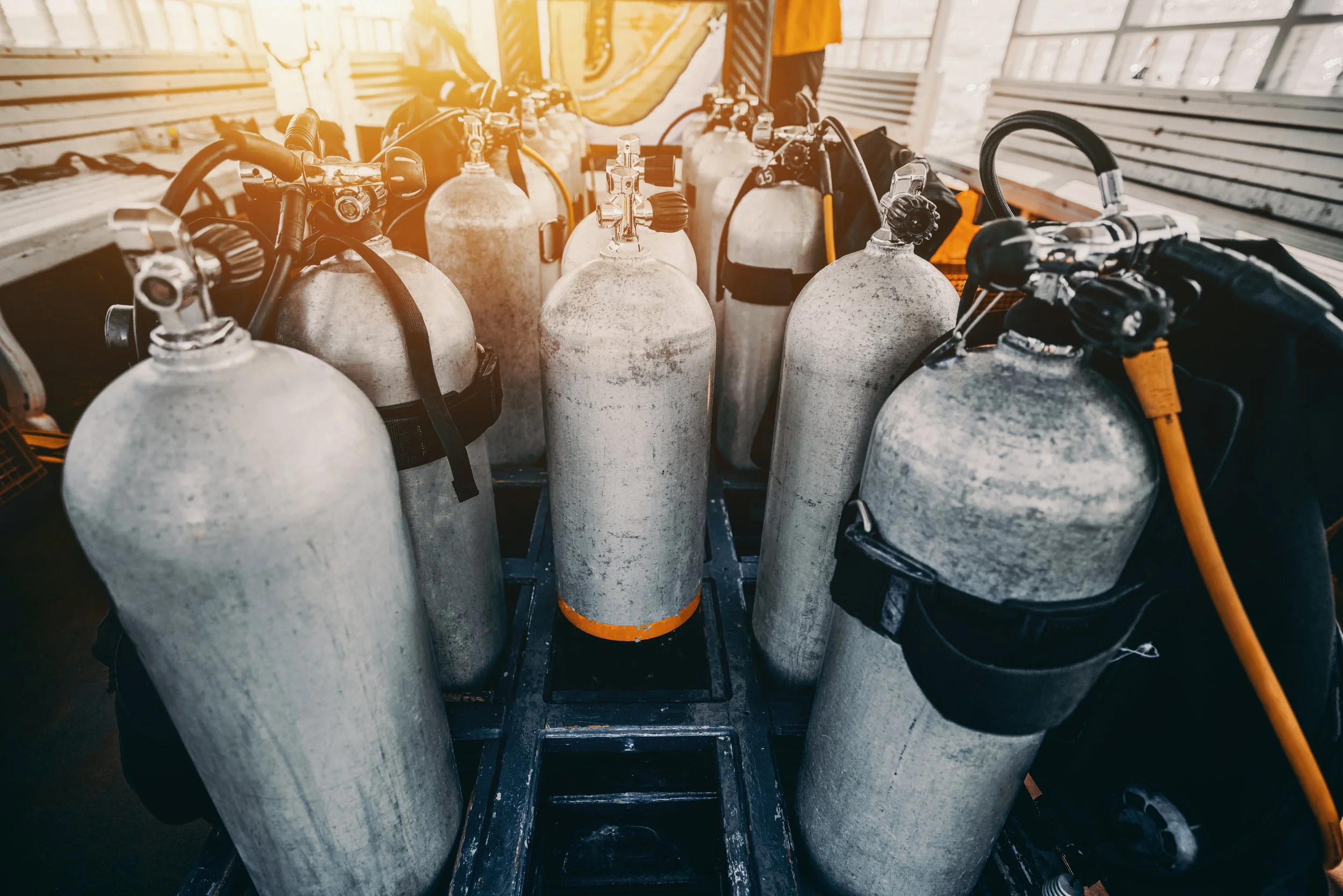 Multiple aluminum scuba tanks with black straps and regulators inside a boat storage area.