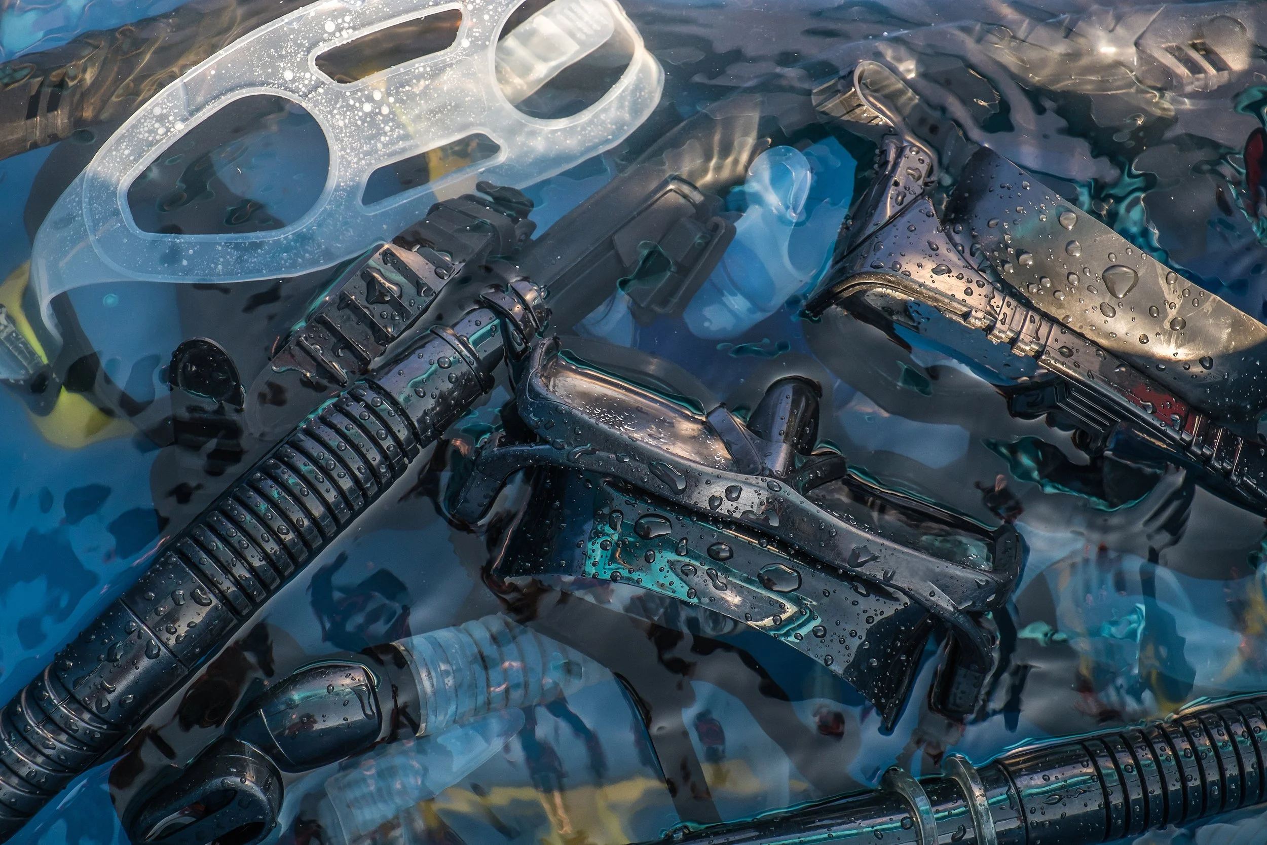 A collection of underwater cameras, torpedoes, and hydration packs submerged in water with droplets on their surfaces.