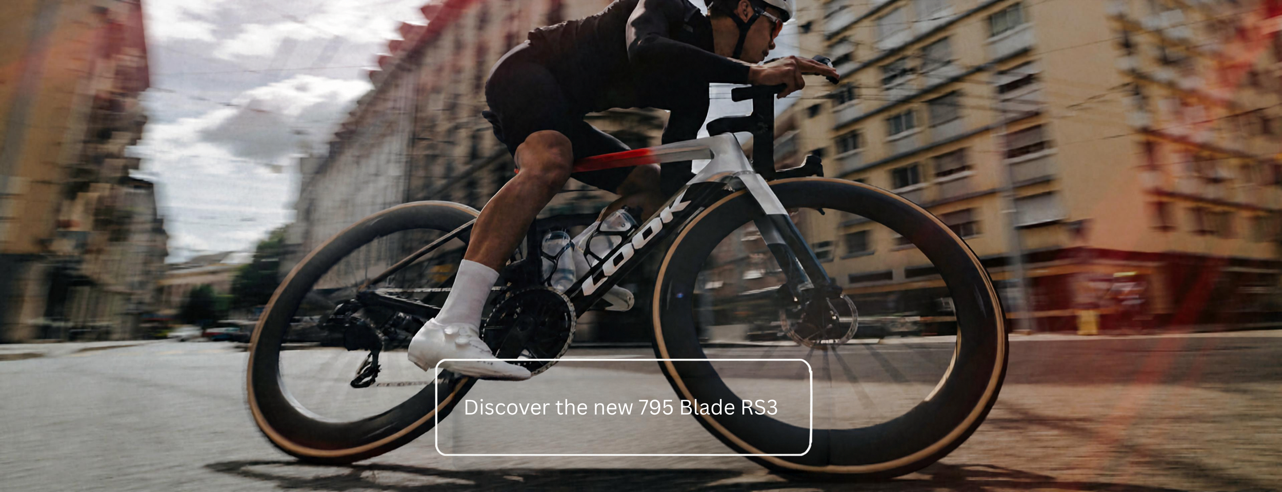 A cyclist wearing a helmet and black clothing riding a black and white bike on a city street with tall buildings in the background. The bike is moving quickly, creating a motion blur, and a text overlay reads: 'Discover the new 795 Blade RS3'.