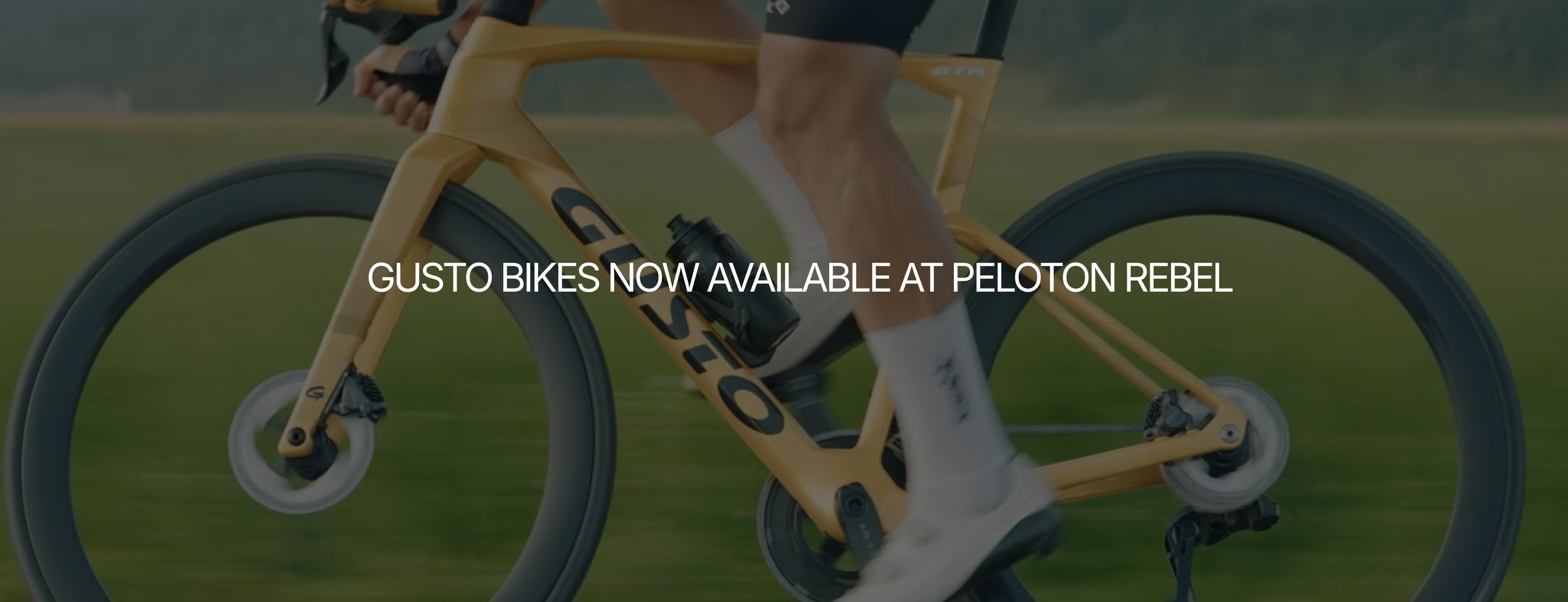 A person riding a yellow Gusto e-bike on grass. The text overlay reads "Gusto Bikes now available at Peloton Rebel."