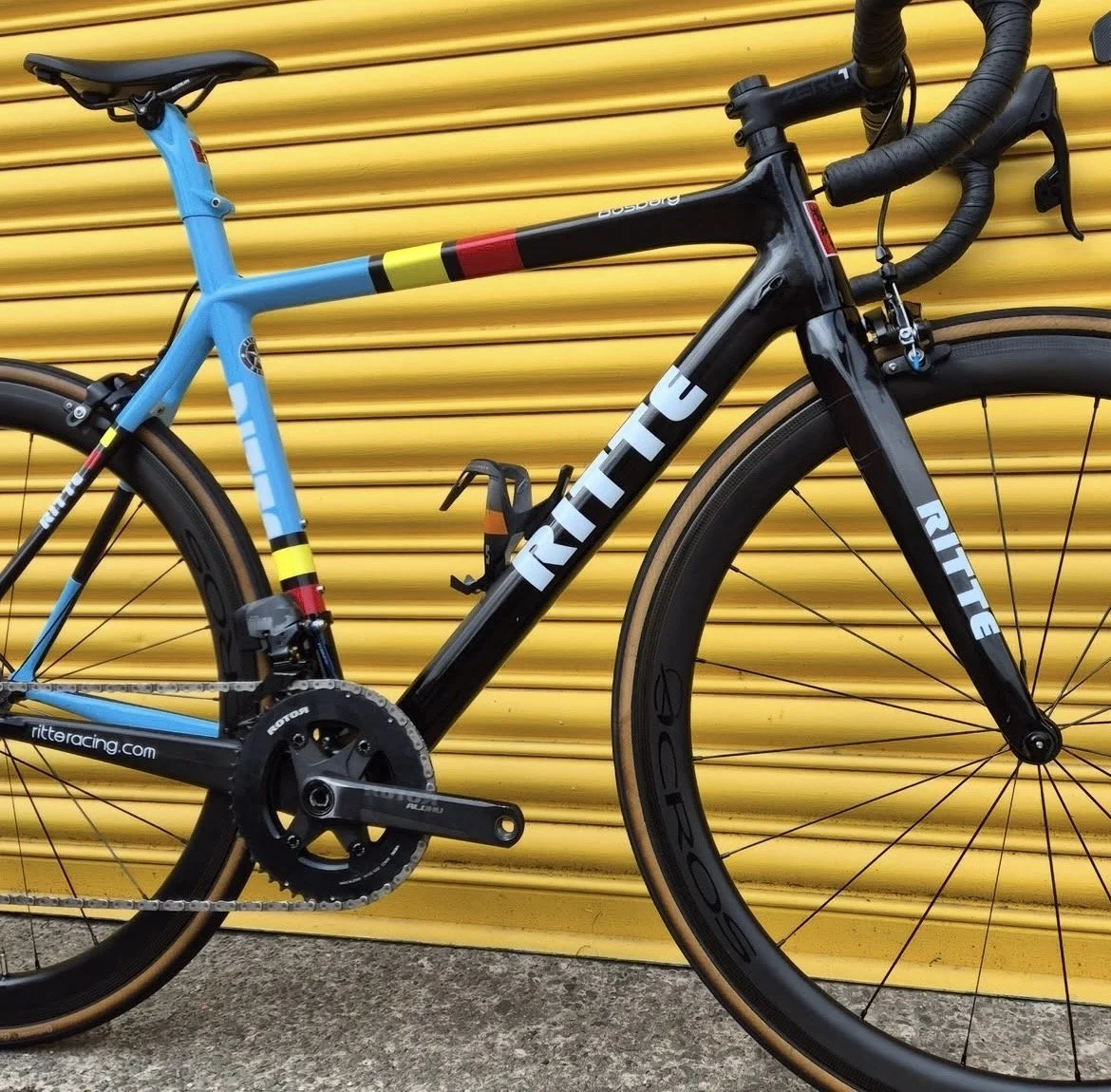 A black and blue road bicycle leaning against a yellow corrugated metal wall.