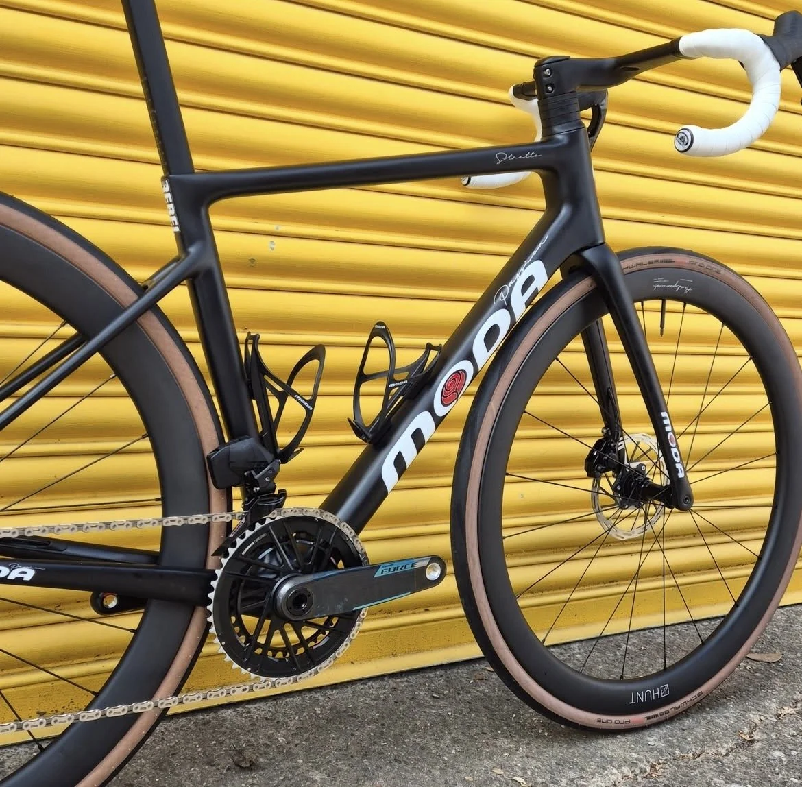 Black road bicycle with tan tires leaning against a yellow roller shutter door.