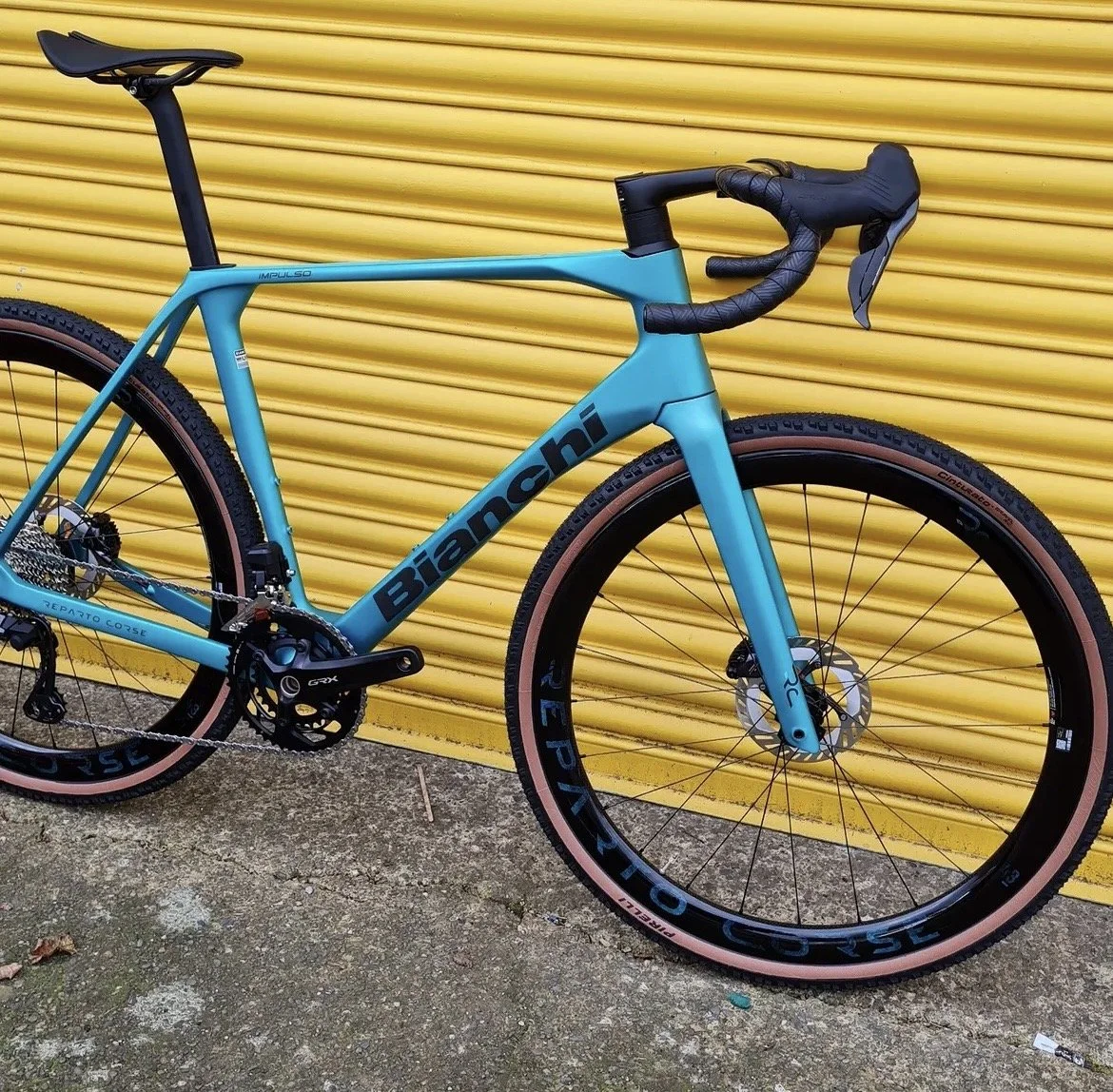 A blue Bianchi road bicycle with black and tan tires, leaning against a yellow corrugated metal wall.