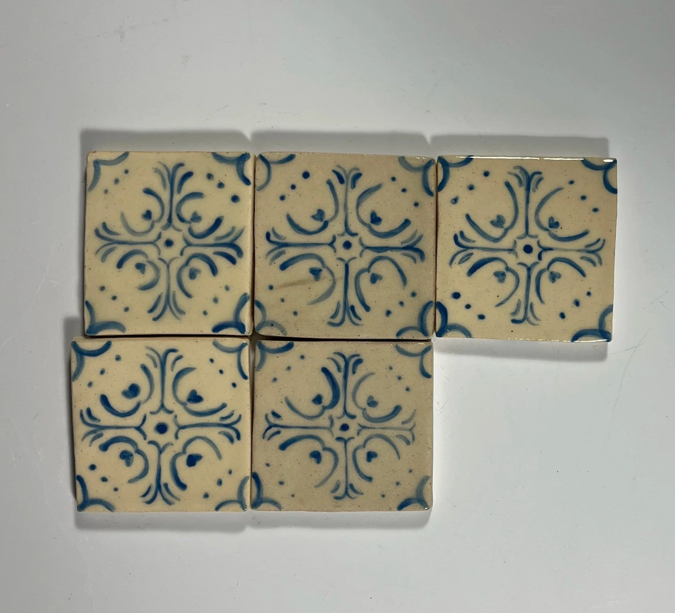 Six decorative ceramic tiles with blue floral patterns arranged in an L shape on a white surface.