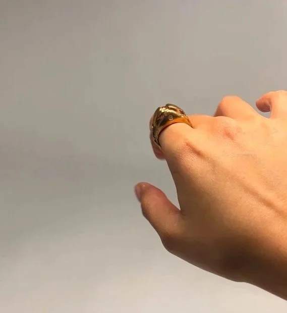 Close-up of a hand wearing two large gold rings, with a plain gray background.