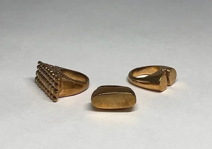 Three gold rings on a white surface, each with unique designs.