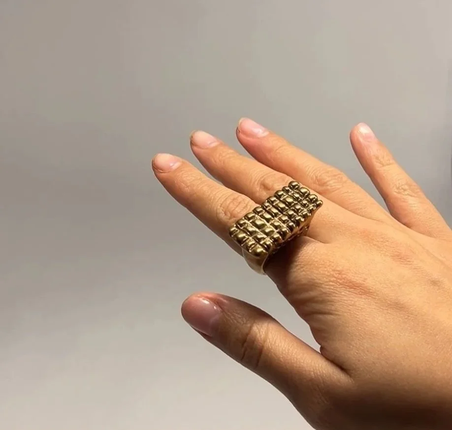 Close-up of a hand wearing a large gold ring with a textured, beaded design.