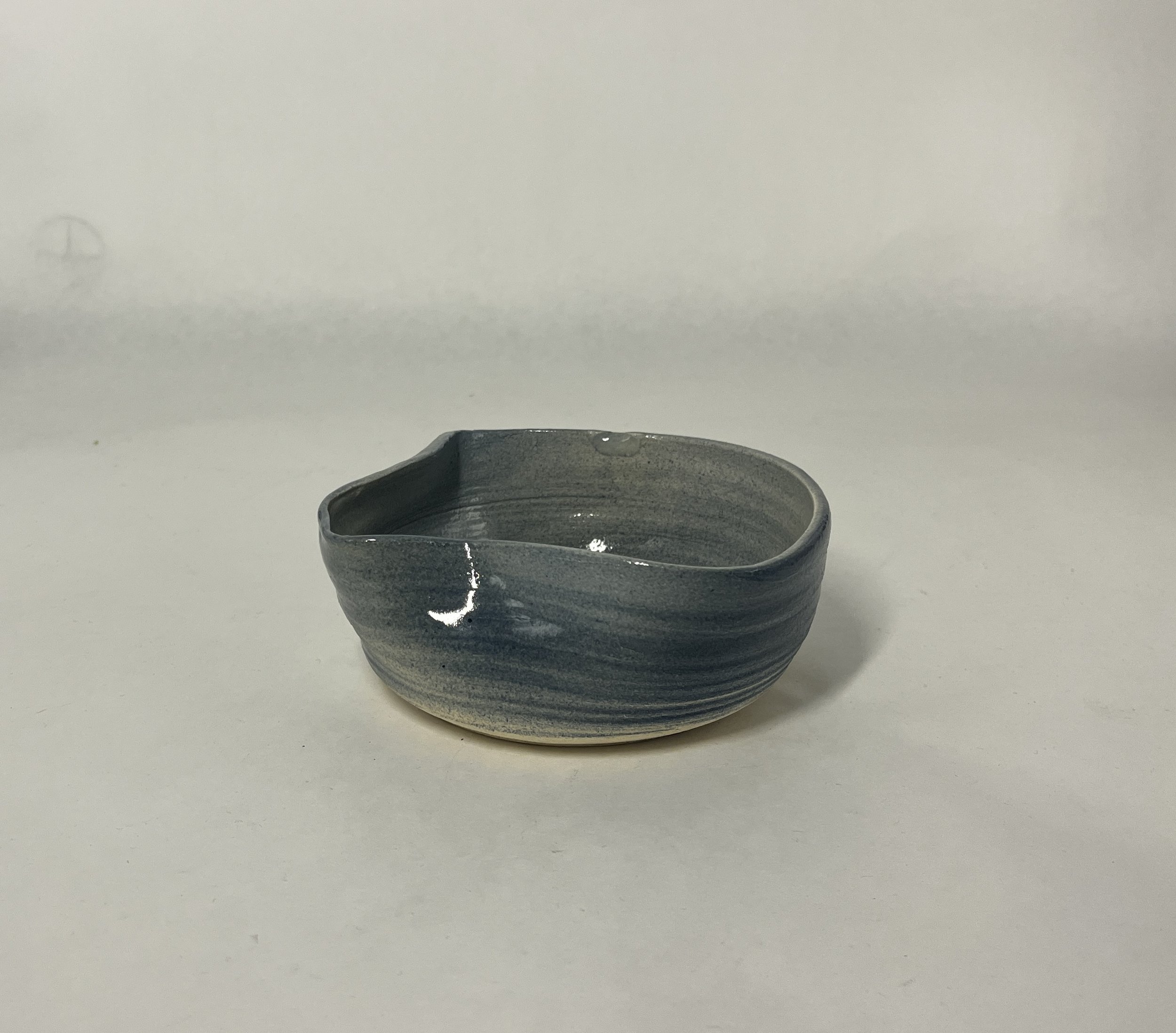 Small, handmade ceramic bowl with a blue and gray glaze on a plain white background.