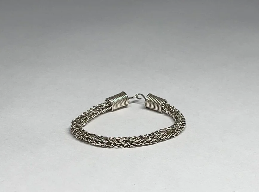 Silver braided chain bracelet with coil ends on a plain light grey background.