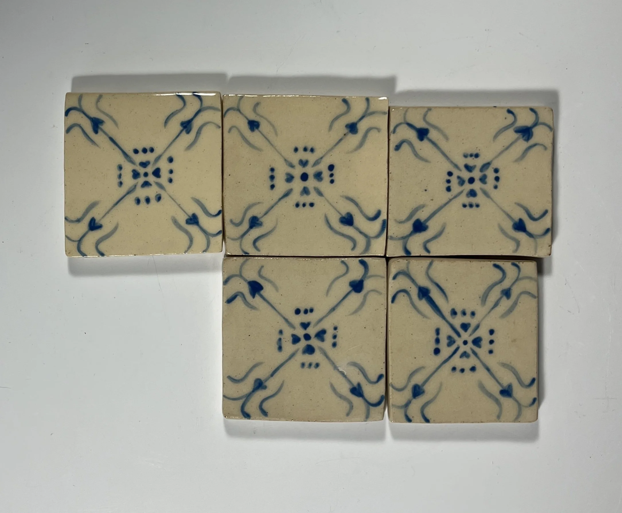 Six decorative ceramic tiles with blue and beige geometric pattern, arranged in a letter 'T' shape on a white surface.