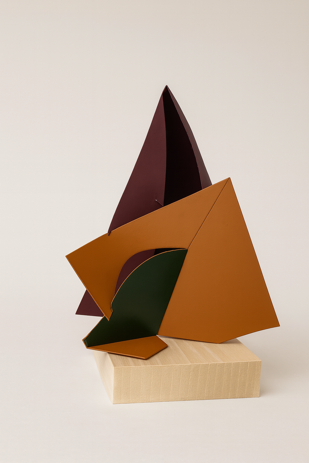Abstract geometric sculpture with angular shapes in shades of orange, green, and dark red on a light wooden base.