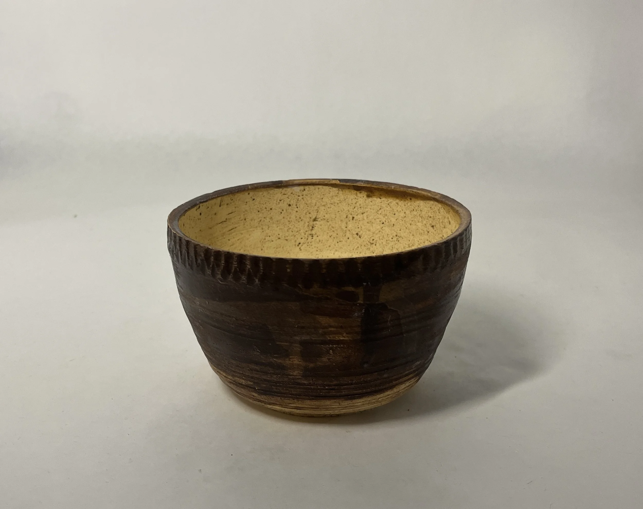 Ceramic bowl with a brown exterior and a cream-colored interior, placed on a plain white surface.