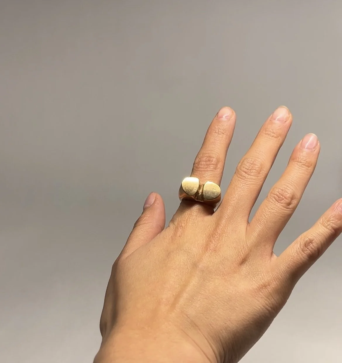 Hand with a large gold ring that has two rounded ends on a plain background.