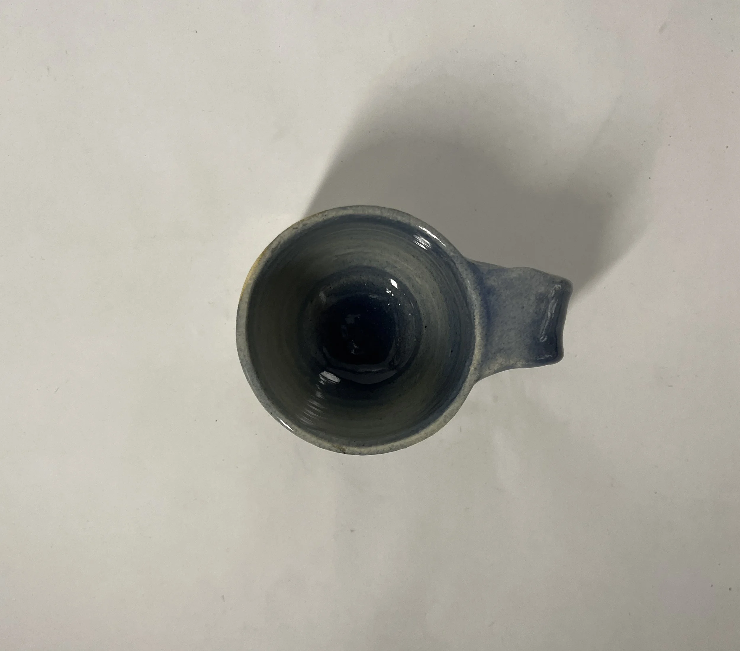 Top view of a ceramic mug with a handle, placed on a white surface, casting a shadow.