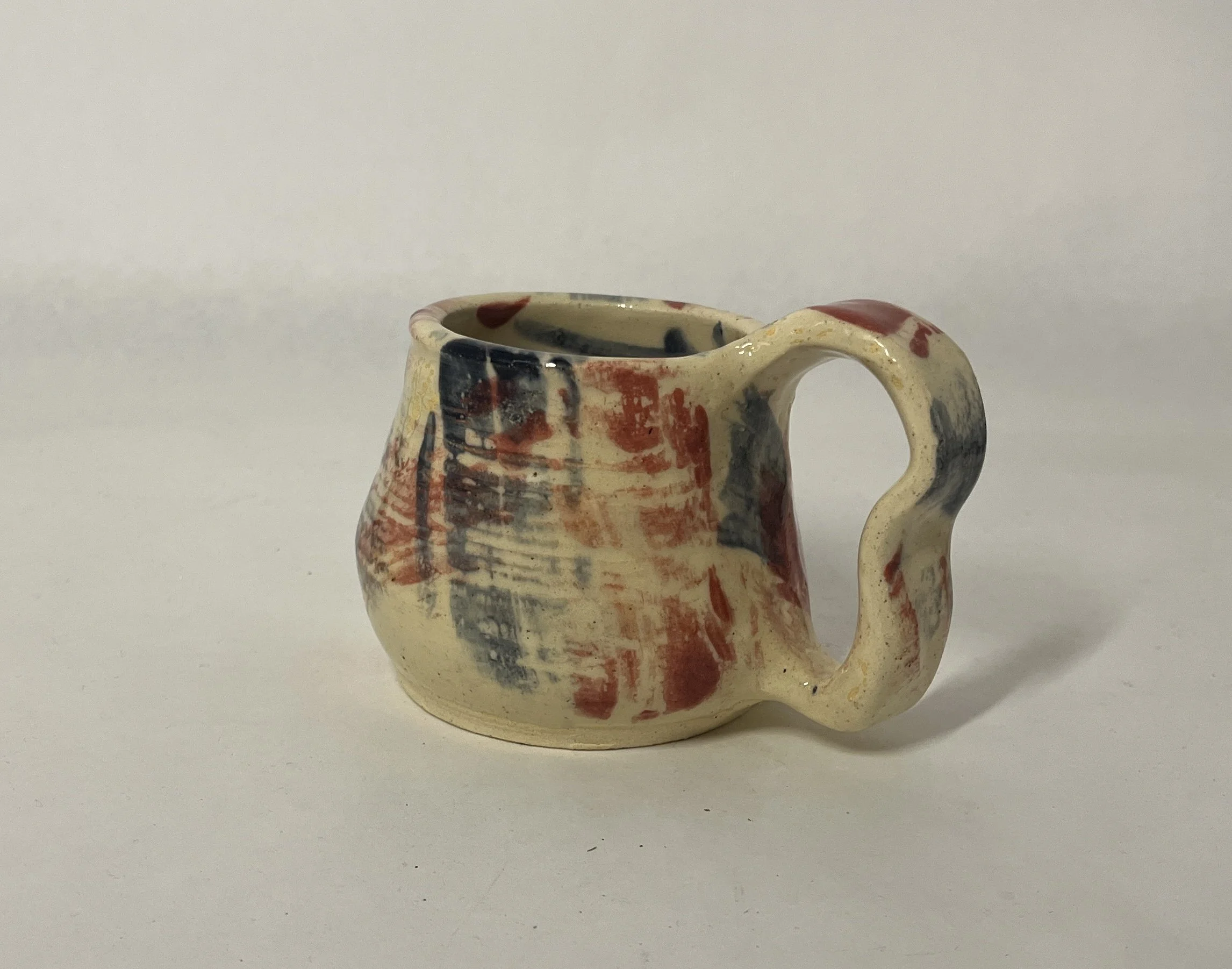 A small ceramic mug with a cream-colored base and abstract red, black, and blue brushstroke patterns