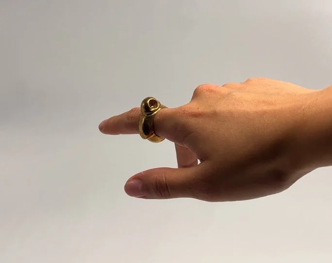 A person's hand wearing multiple gold rings, with the index finger extended and pointing to the right against a plain white background.