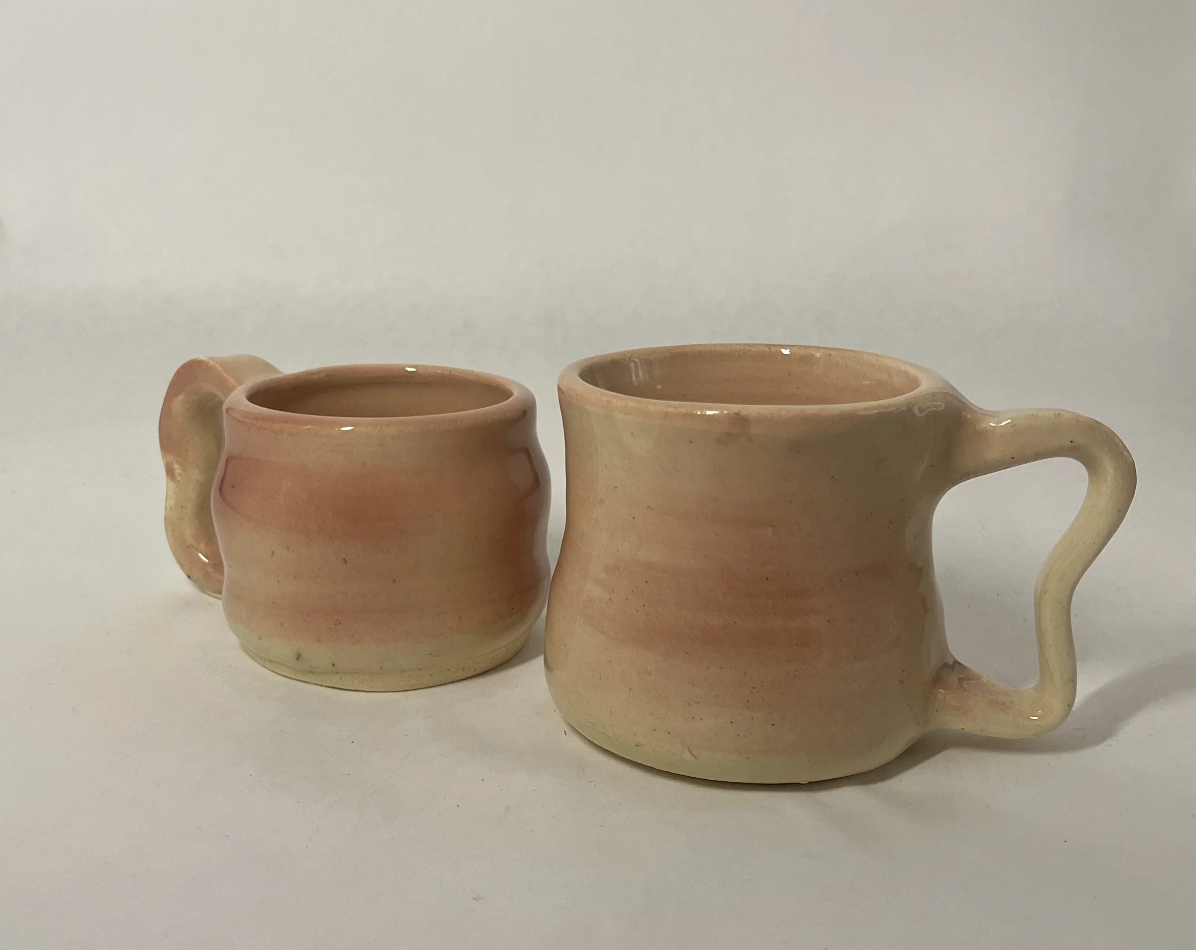 Two handcrafted ceramic mugs with pastel pink and beige gradient glaze on a white background.