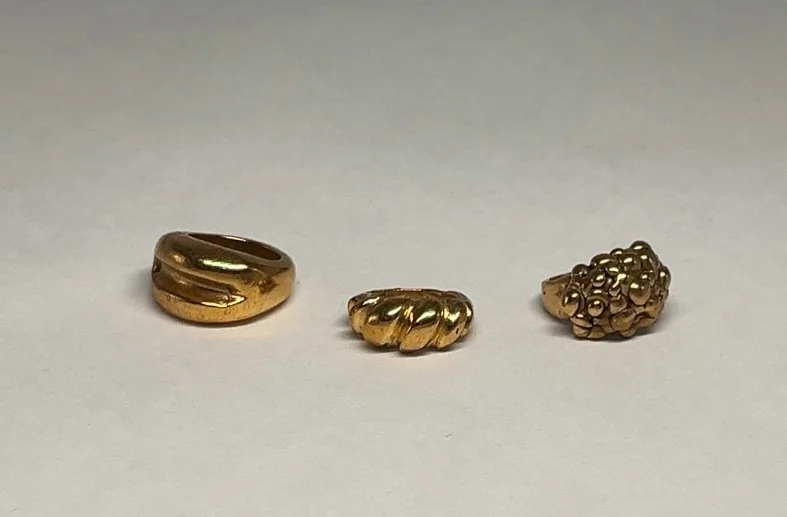 Three gold rings with different designs placed on a plain white surface.