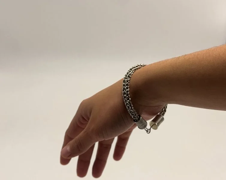 A hand wearing a metallic chain bracelet with a coil and clasp, extending outward against a plain light background.