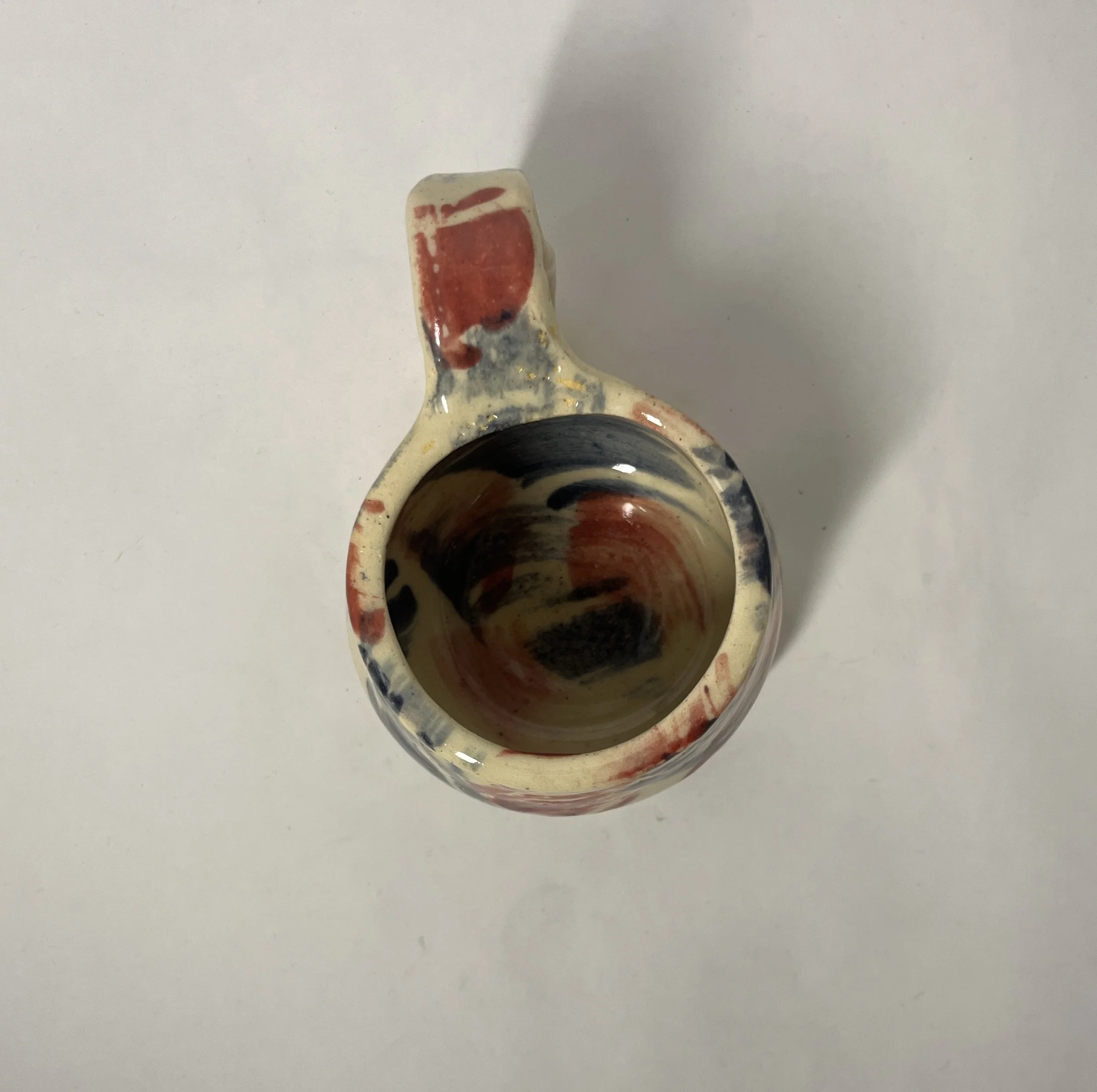 A ceramic vase with multicolored swirling pattern, viewed from above on a white surface.