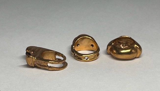 Three gold jewelry clasps or findings on a plain surface.