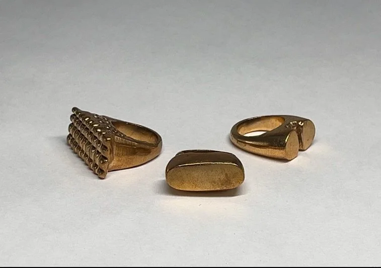 Three gold rings on a white surface, each with unique designs.