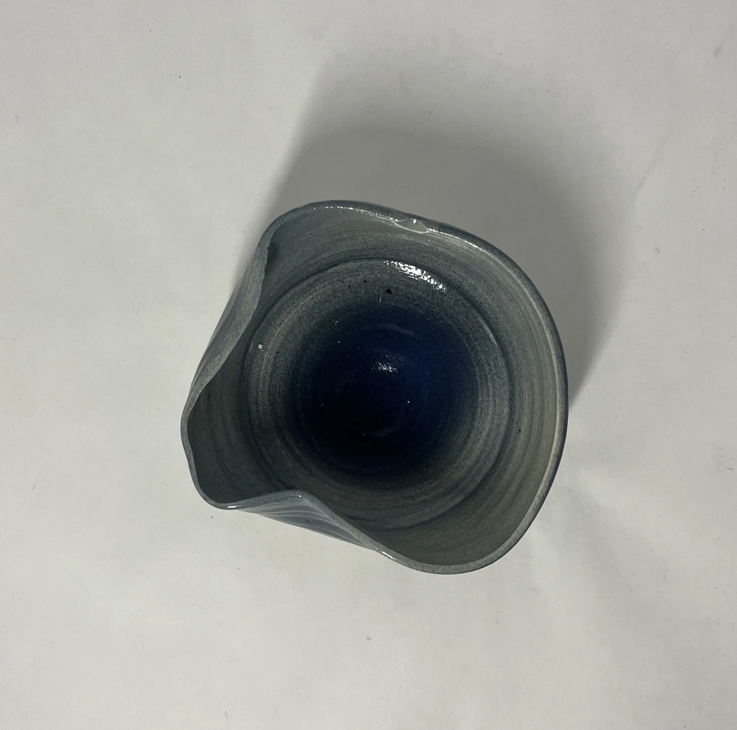 Top view of a ceramic vase with a narrow opening, featuring a gradient of gray and black colors, placed on a white surface.