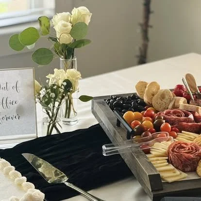 Charcuterie platter with cheeses, meats, cherry tomatoes, and crackers on a table with white roses