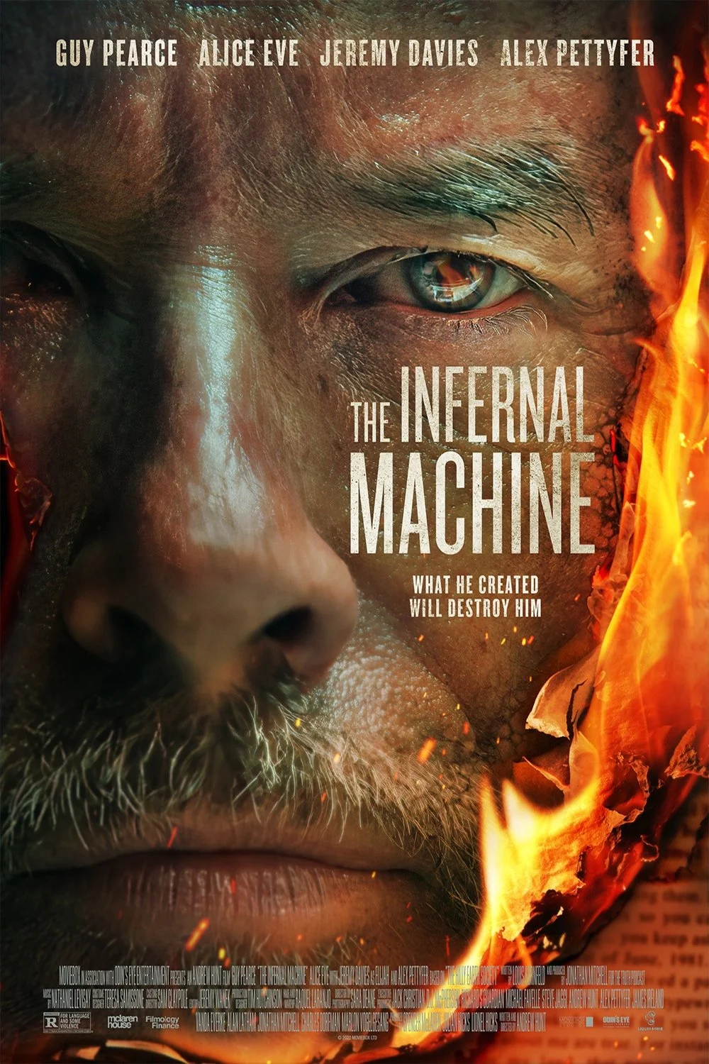 Close-up of a man's face with intense eyes, one eye reflecting a fiery scene, surrounded by flames, promoting the movie 'The Infernal Machine'.