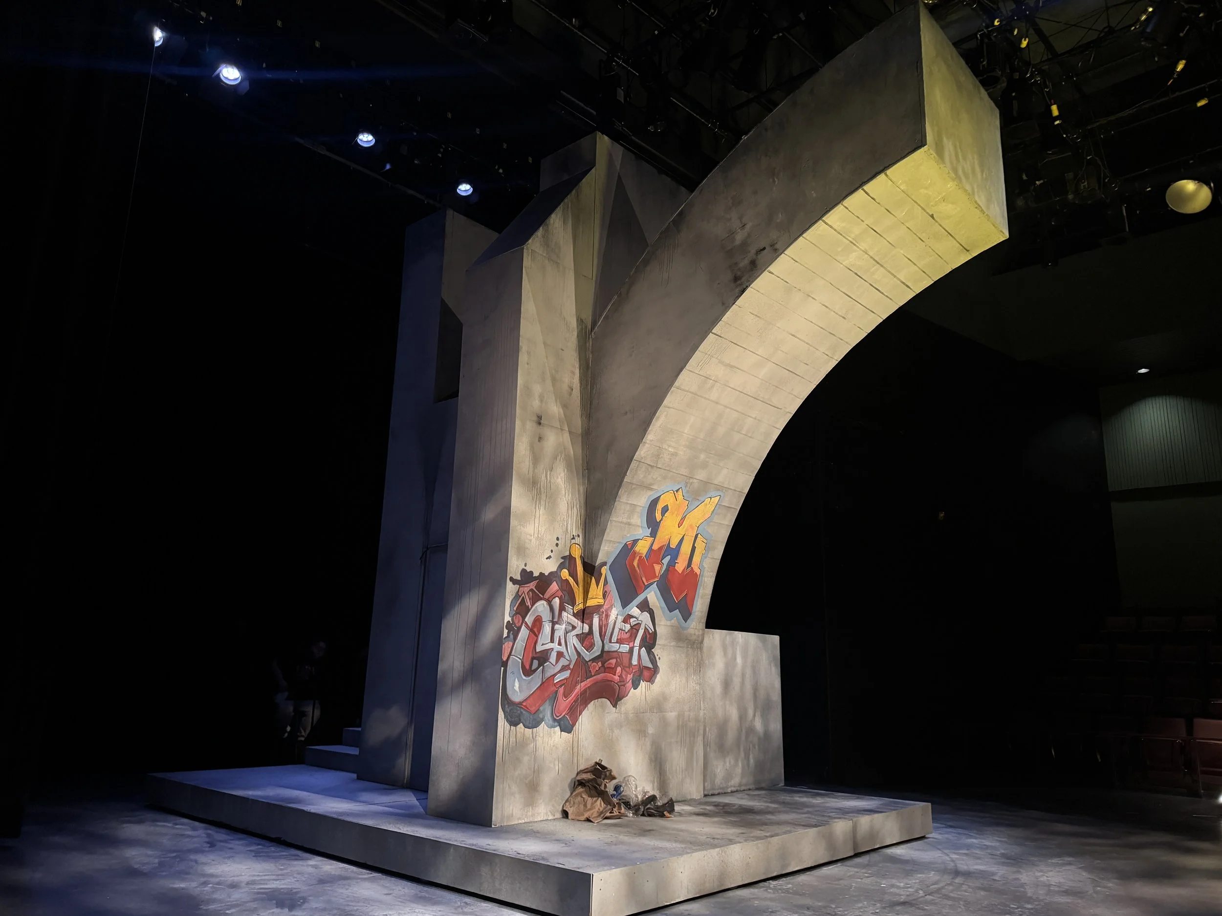 A concrete stage with graffiti art at the center, set against a black background in a dark theater.