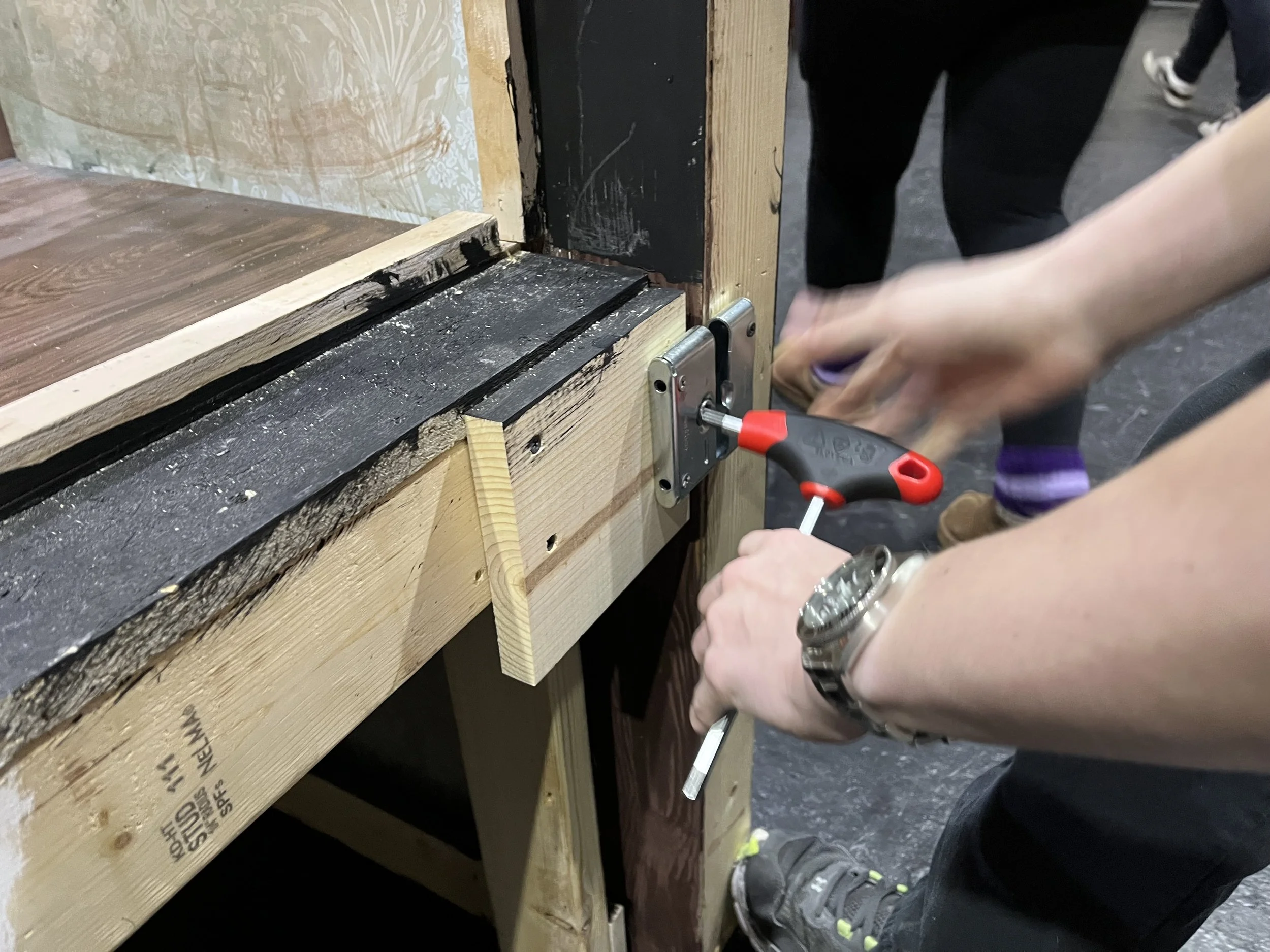 Person using an allen wrench to assemble a wooden structure, with a focus on their hands and the tool, in an indoor setting.