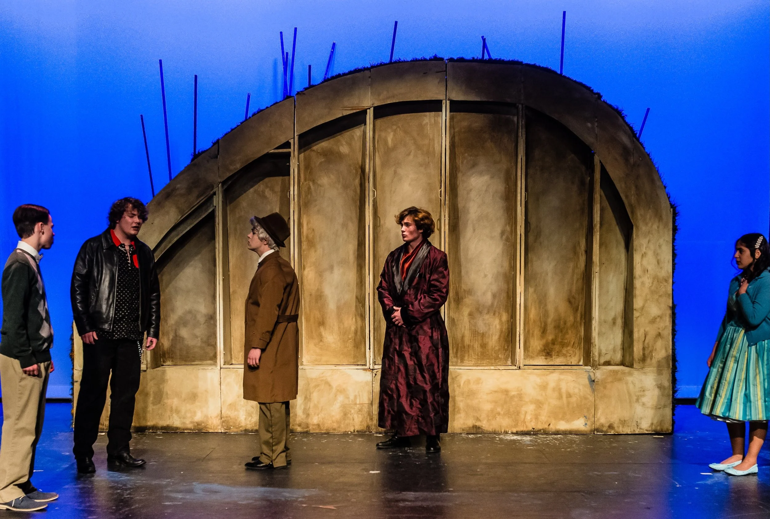 A one-act production of Midsummer Night's Dream. Six actors on stage, five men and one woman, dressed in vintage clothing, standing in a semi-circle with a brown, dome-shaped set piece in the background and blue lighting.