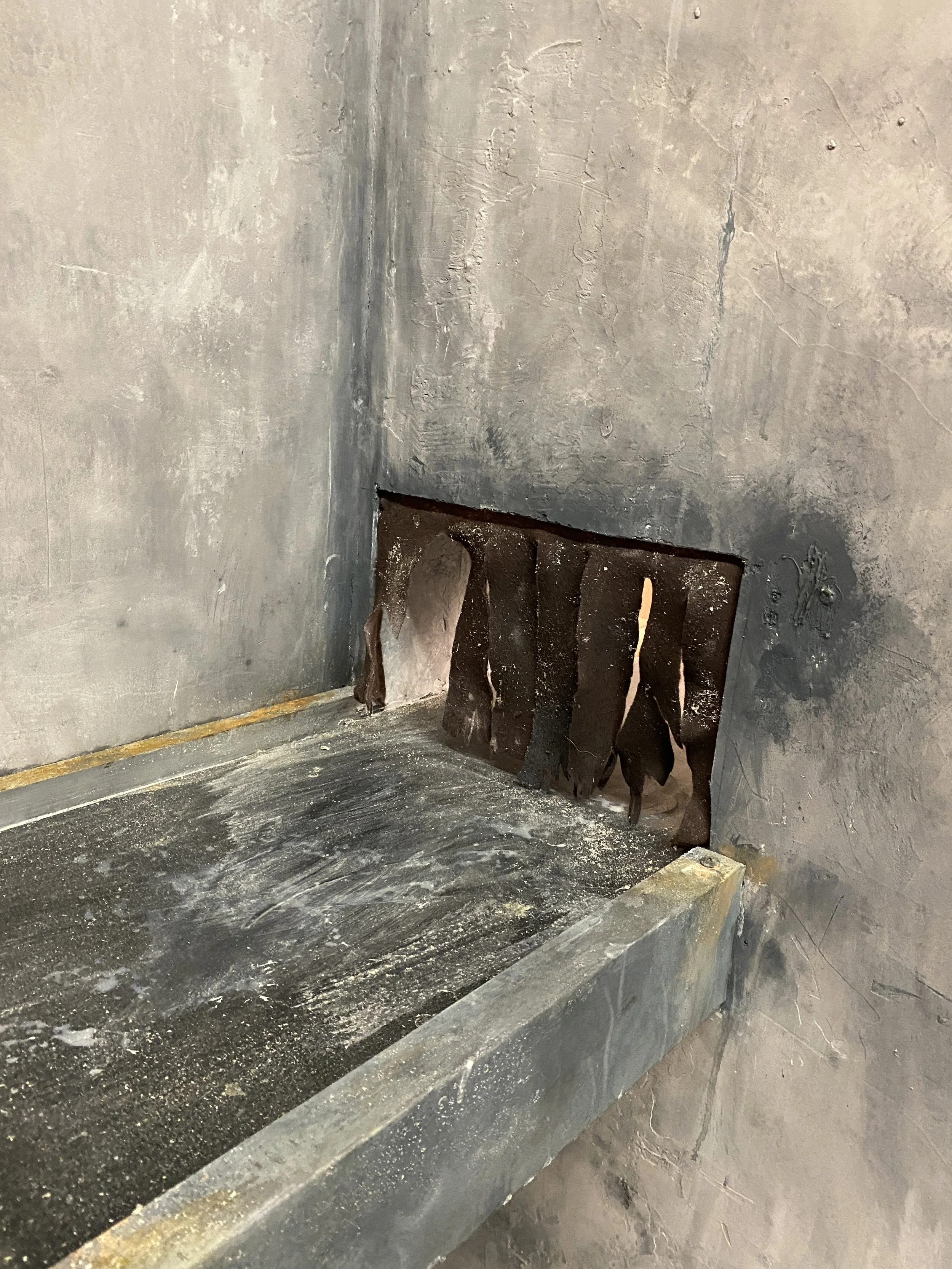 A close-up of a blackened conveyor belt inside a sooty, unfinished concrete wall.