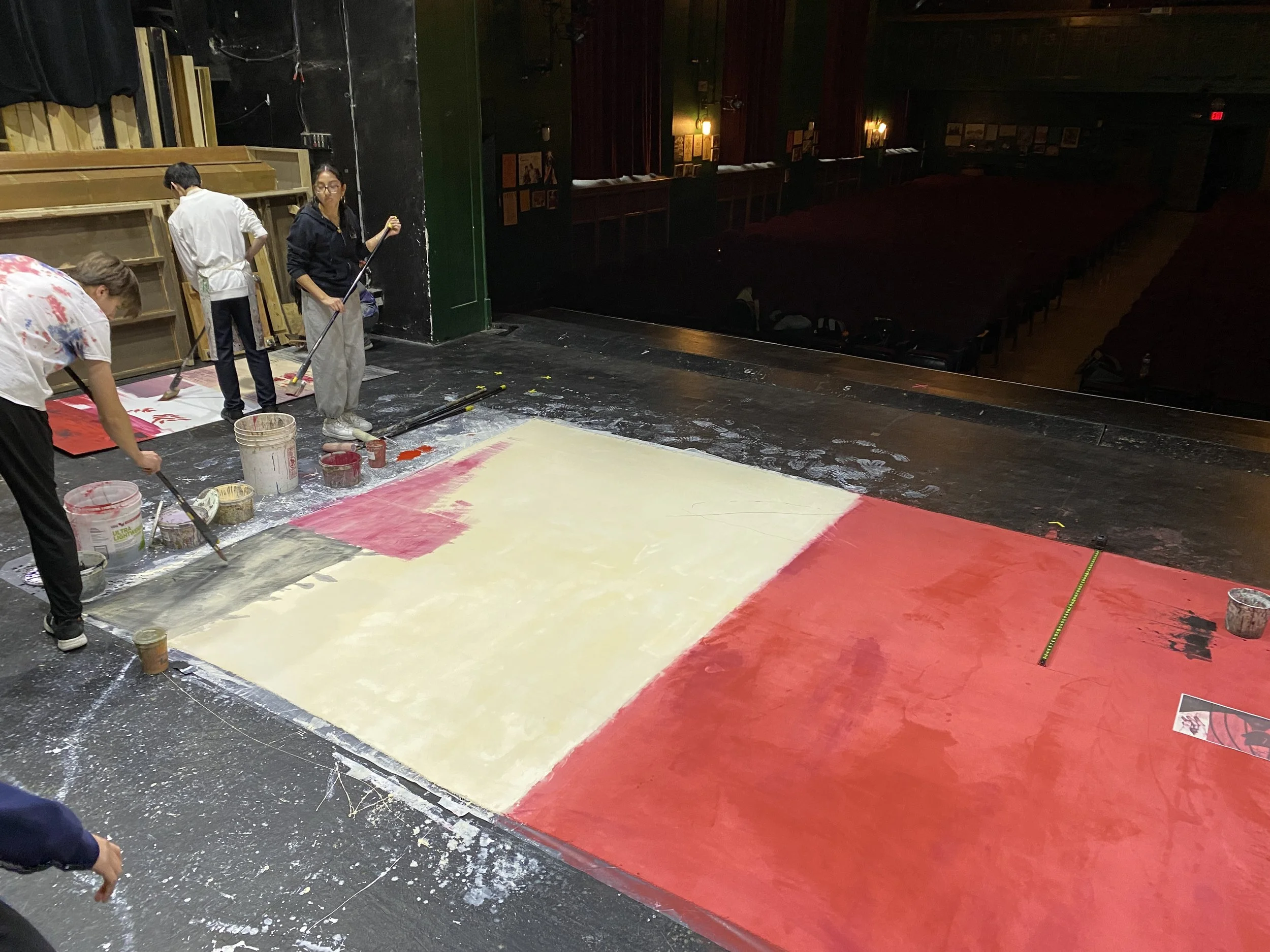 People painting a large stage backdrop with red and yellow sections.