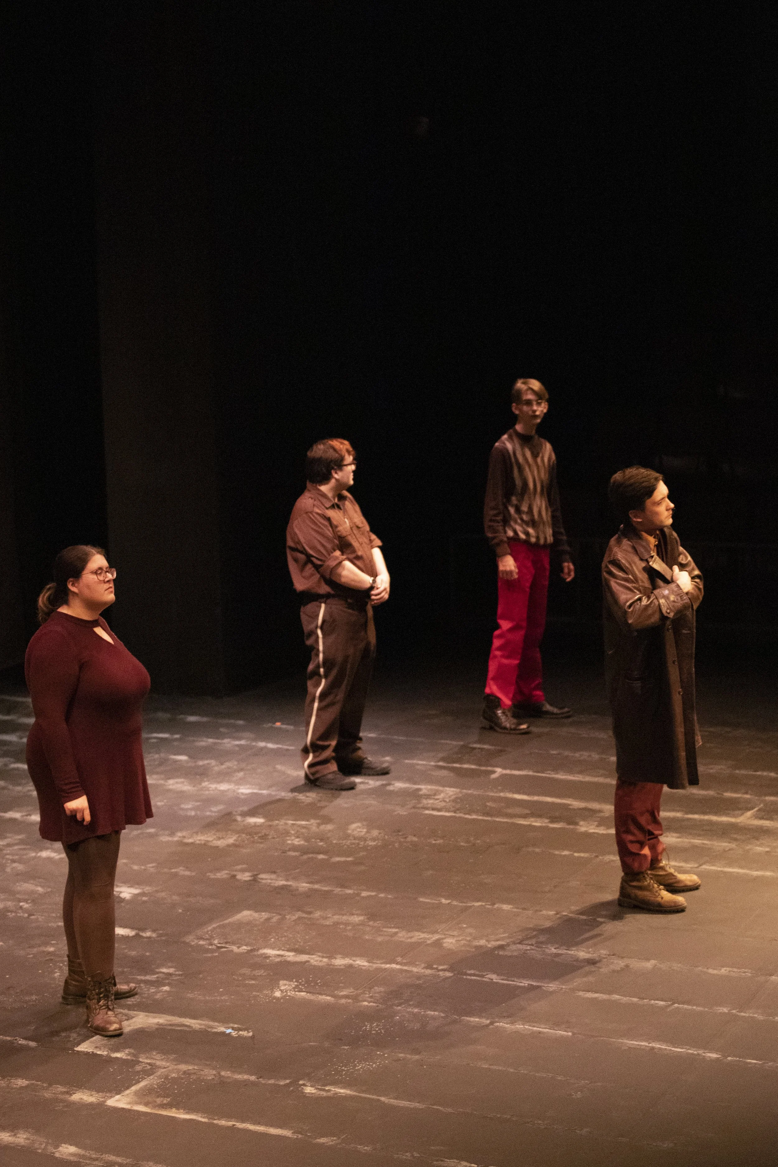 Five people standing on a dark stage, spaced apart, facing similar directions, with a black background.