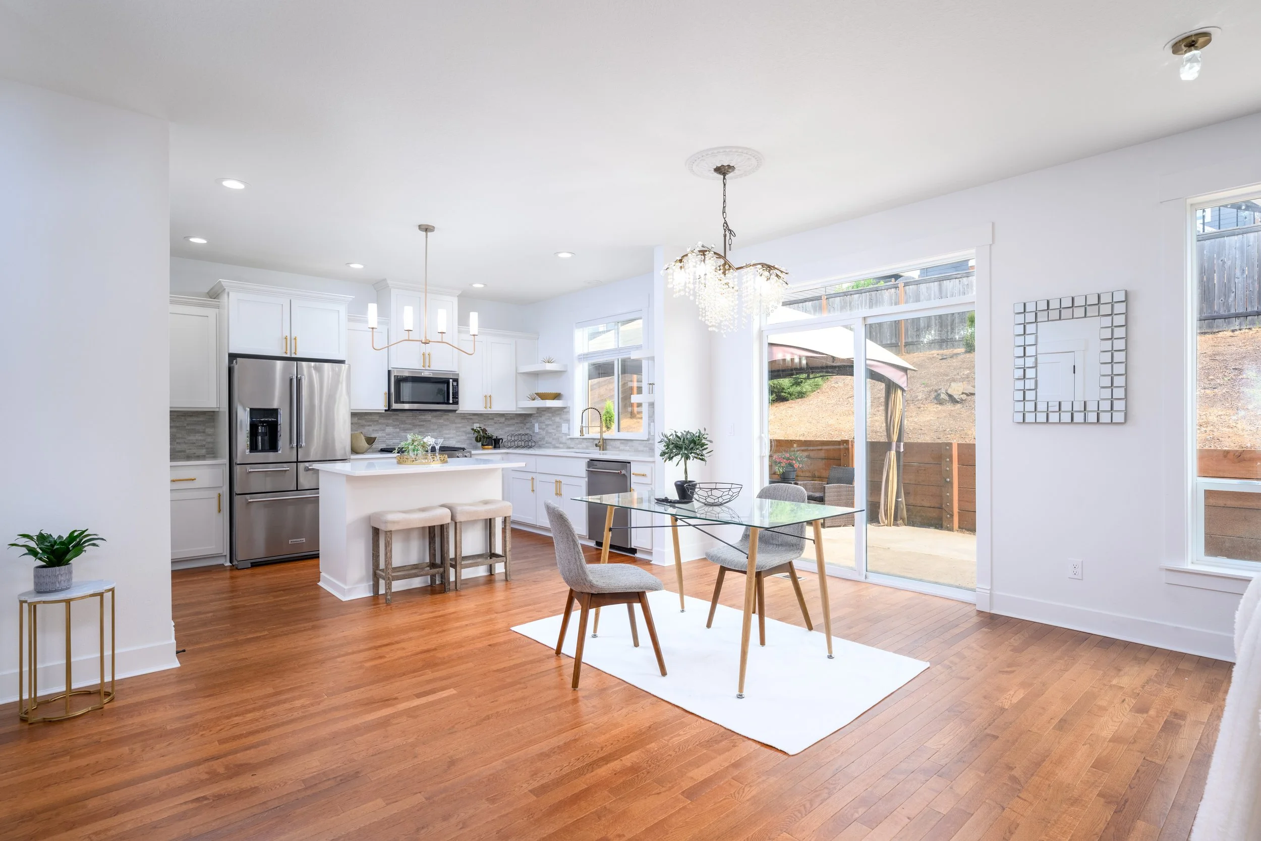 Open concept kitchen and dining area with white cabinets, stainless steel appliances, hardwood floors, and large windows providing natural light.