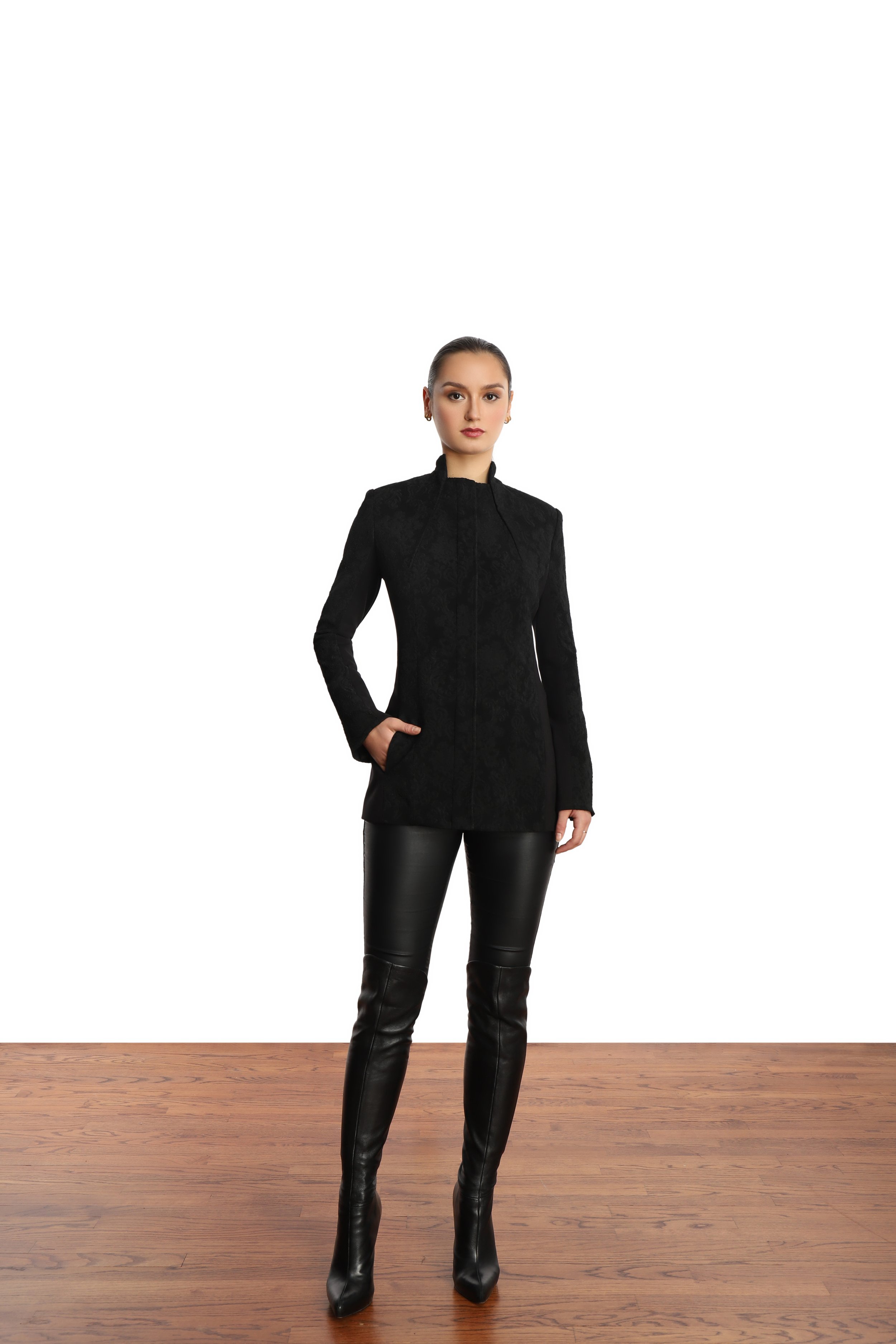 Model with slick back ponytail, wearing a black blazer and black shiny wet look leggings and thigh high black boots. 