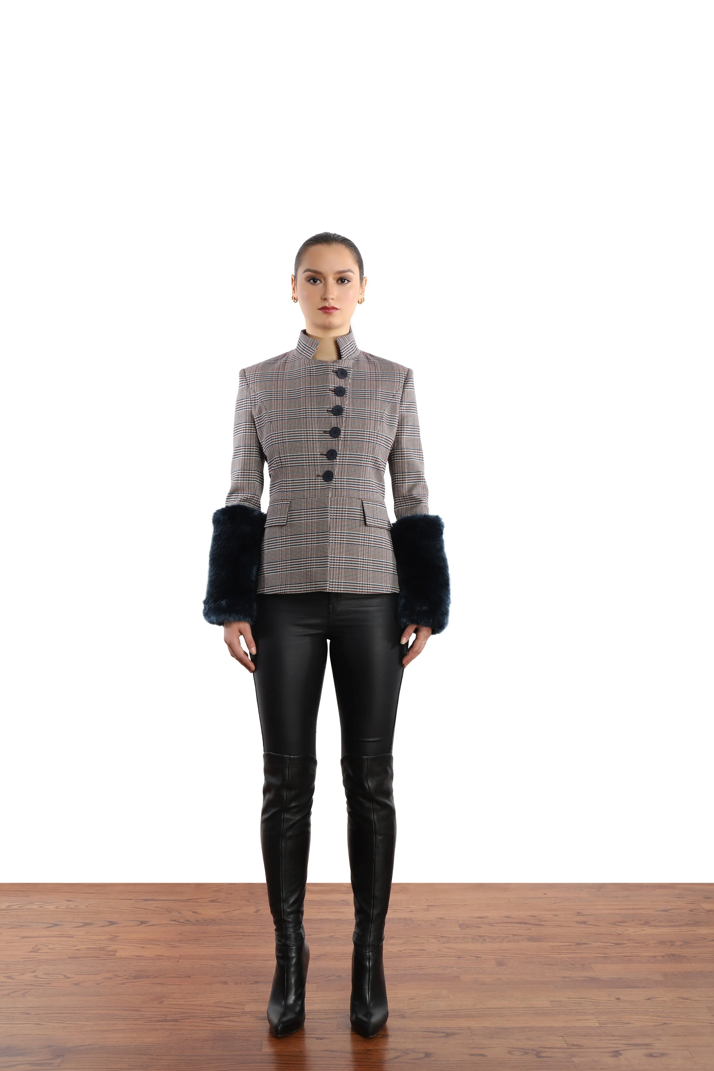 Model with slick back ponytail, wearing a grey glen plaid blazer with faux fur cuffs. Black leather-like leggings and thigh-high leather boots. 