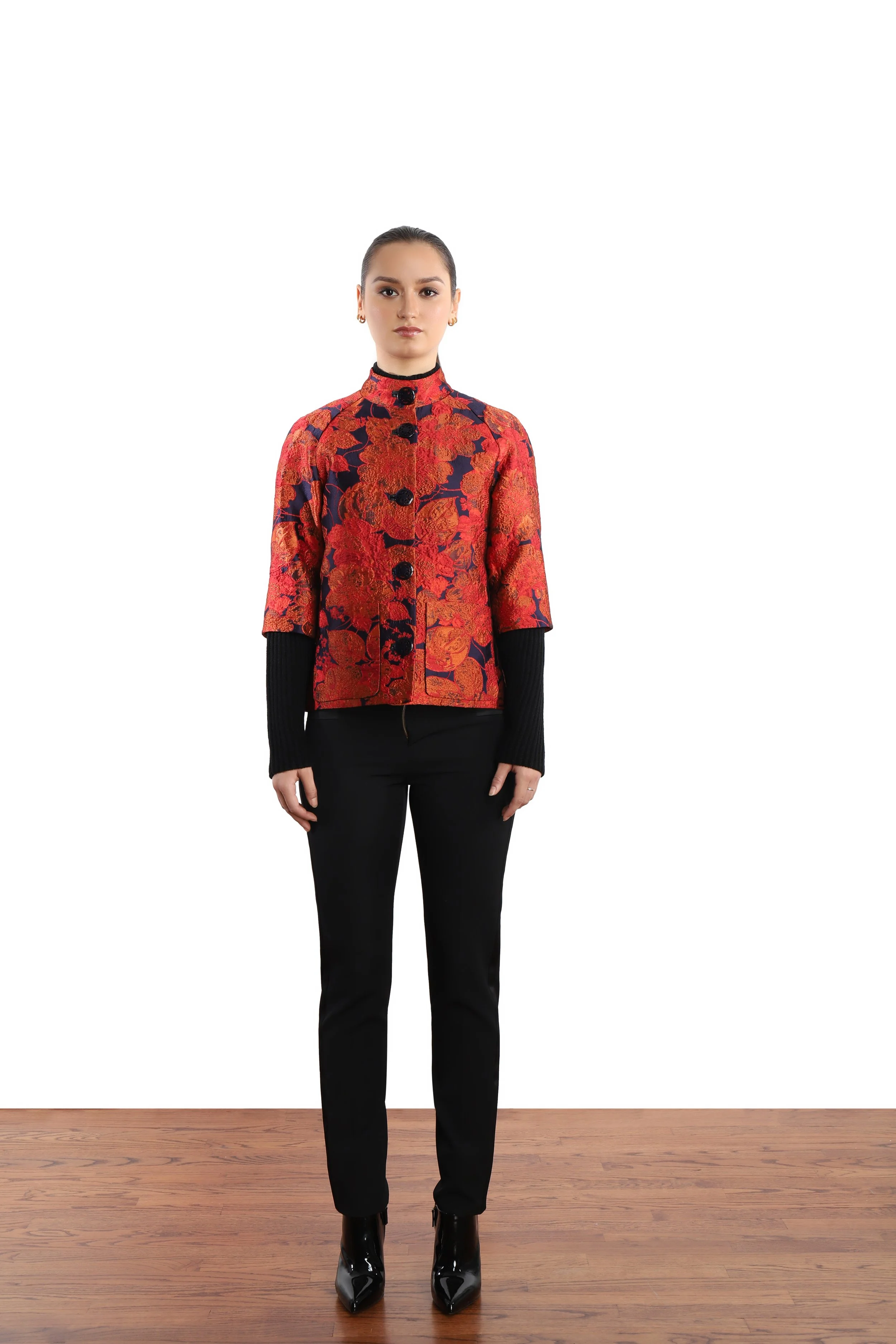 Model wearing a red and black floral embroidered floral blazer with black rib knit sleeves, leather-like black pants and black boots.