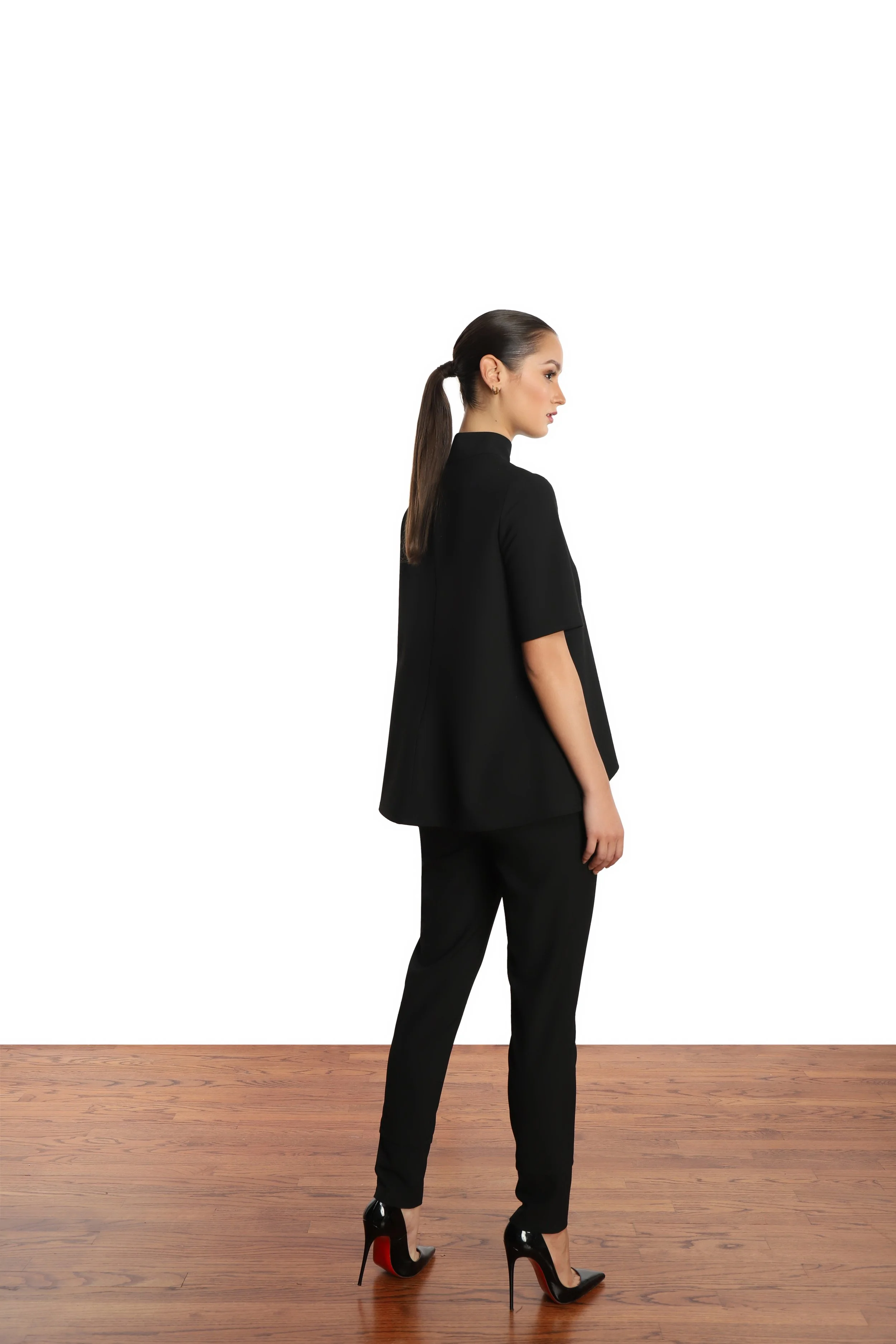 Model with slick back ponytail wearing a-line short sleeve blouse, black pants, and black patent leather stilettos.