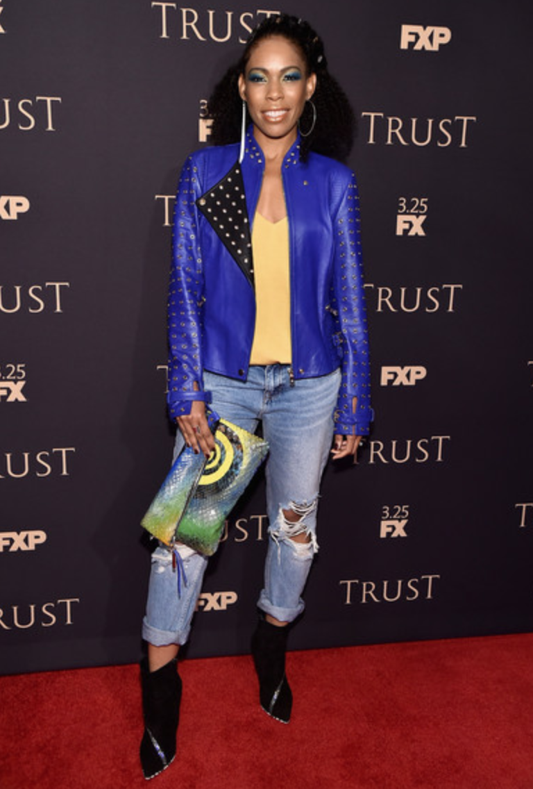 Angela Lewis, on the red carpet at the FX Snowfall party wearing a blue leather jacket and jeans, styled by Chandra Moore.