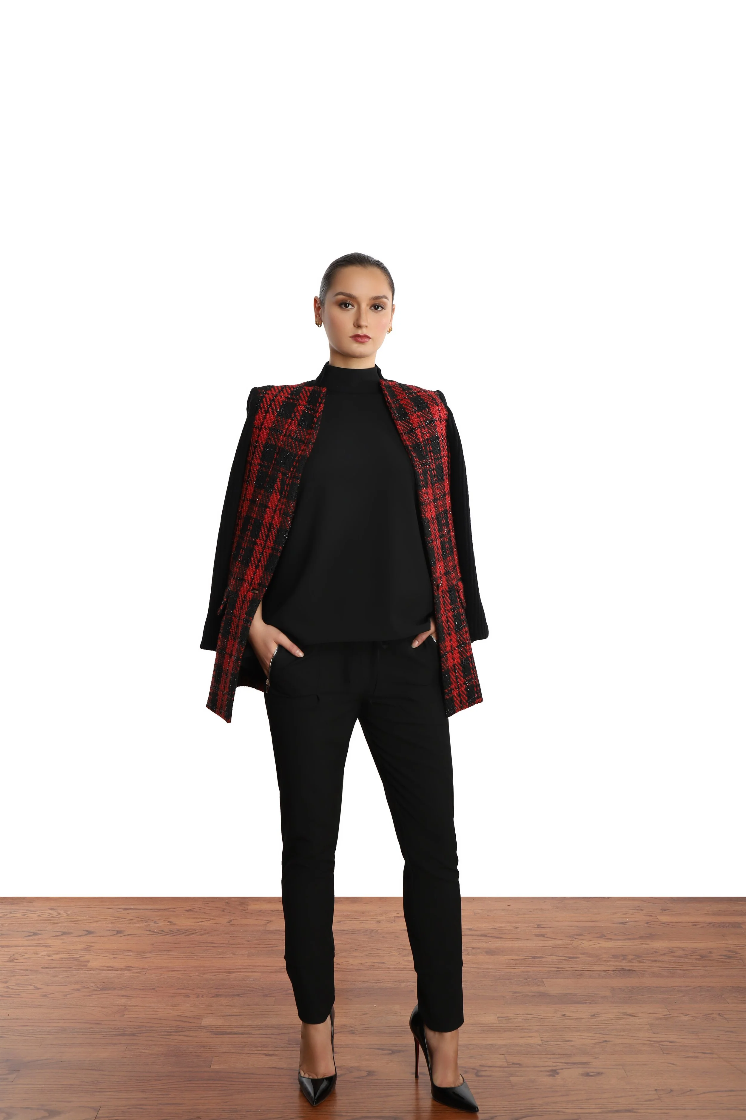 Model with slick ponytail, wearing black and red plaid blazer with black top and pants and patent leather black stilettos. 