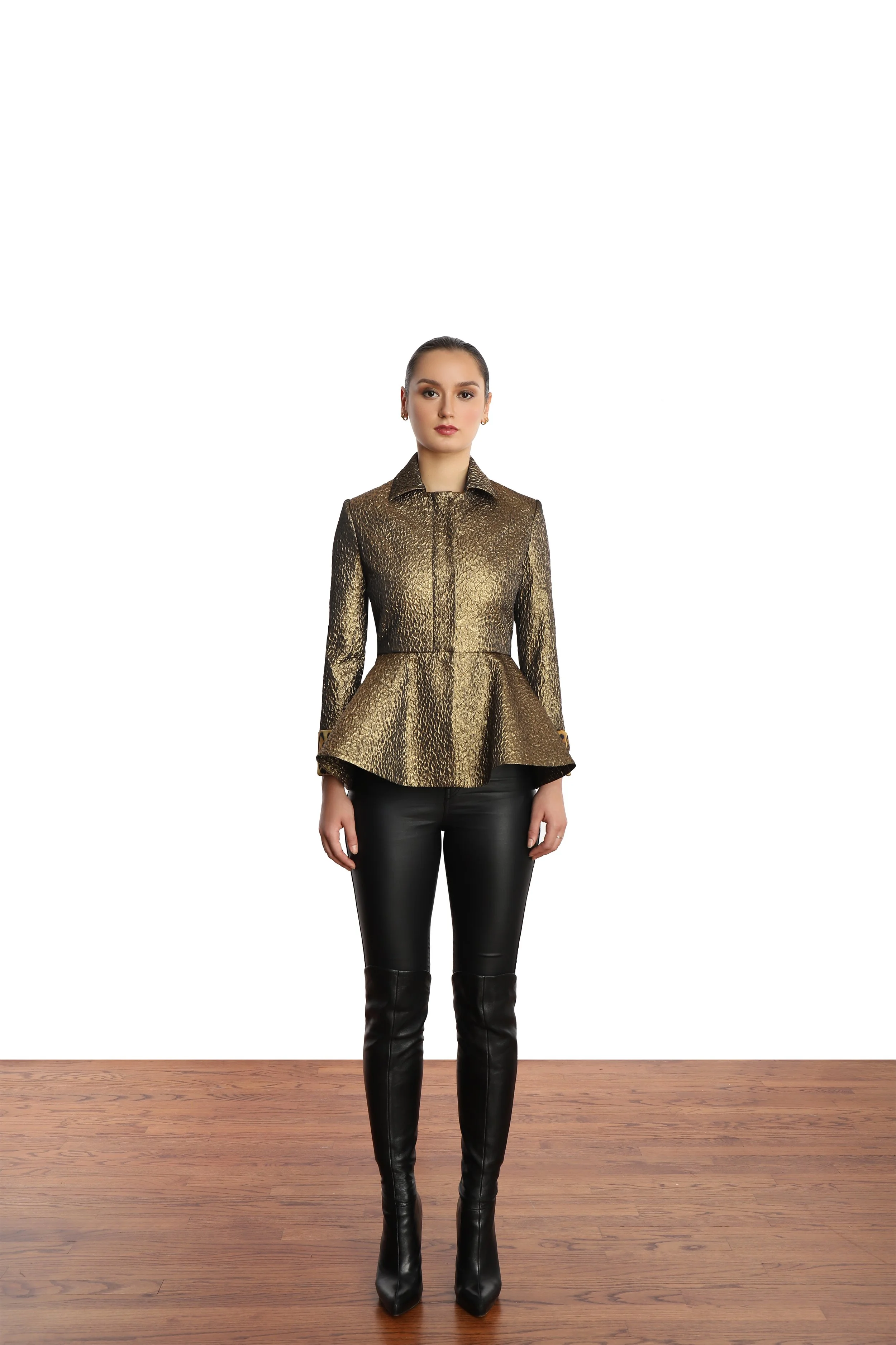 Model with slick ponytail, wearing a mettalic gold blazer with peplum detail and black leather like leggings and black stiletto short boots. 