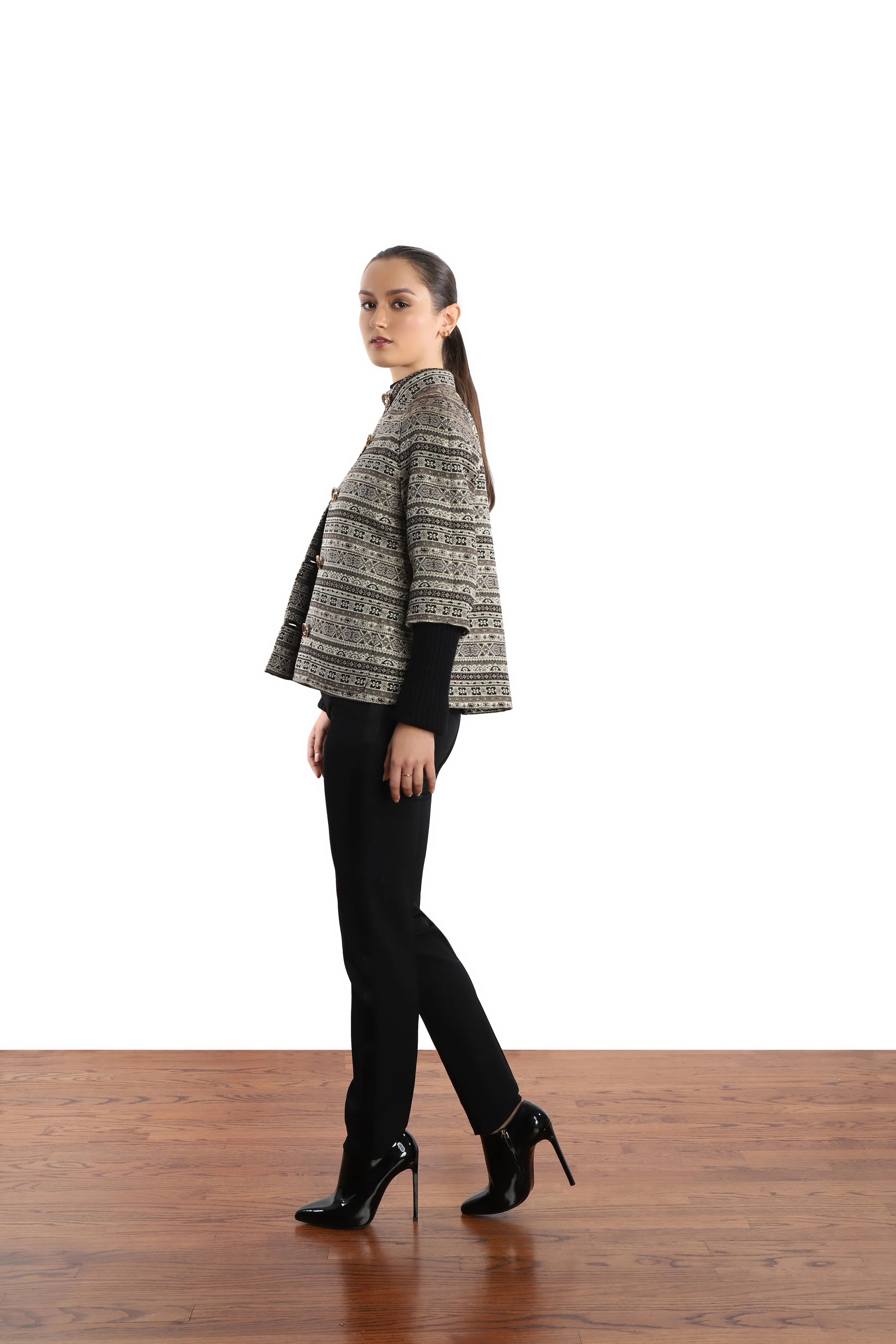 Model in slick ponytail wearing woven swing jacket, black pants and leather high heel booties. 